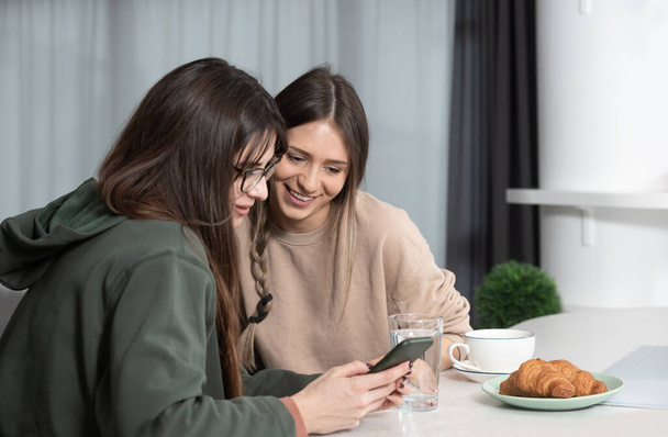 Young woman visiting her friend in her new cozy modern studio apartment, talking about men and relationships. Females students roommates chatting and gossiping. - Fotó, kép