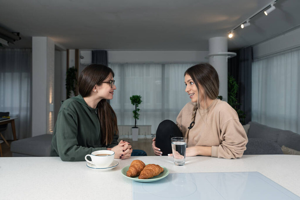 Young woman visiting her friend in her new cozy modern studio apartment, talking about men and relationships. Females students roommates chatting and gossiping. - 写真・画像