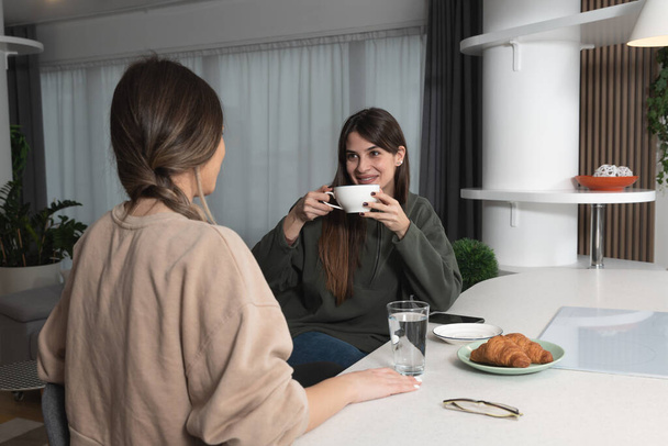 Young woman visiting her friend in her new cozy modern studio apartment, talking about men and relationships. Females students roommates chatting and gossiping. - Foto, Imagem
