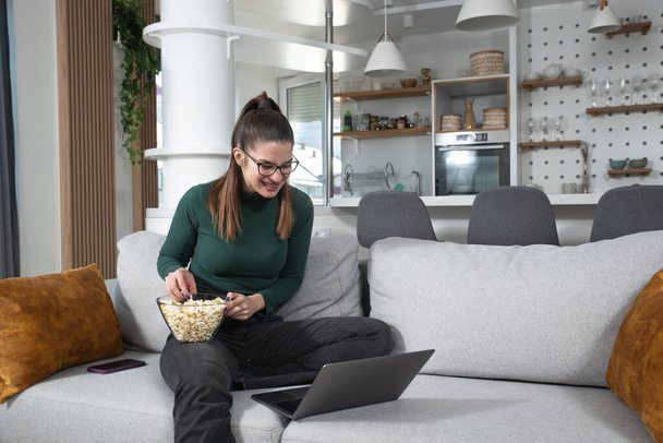 Smiling young woman using laptop, sitting on couch at home, beautiful girl shopping or chatting online in social network, having fun, watching movie, freelancer working on computer project - Φωτογραφία, εικόνα