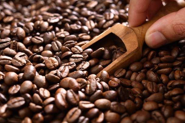 Elle kahve çekirdeğini büyük bir kahve çekirdeğinden ahşap kaşık kullanarak toplamak. Aromatik taze kavrulmuş kahve çekirdekleri yığından çıkarılıyor.. - Fotoğraf, Görsel