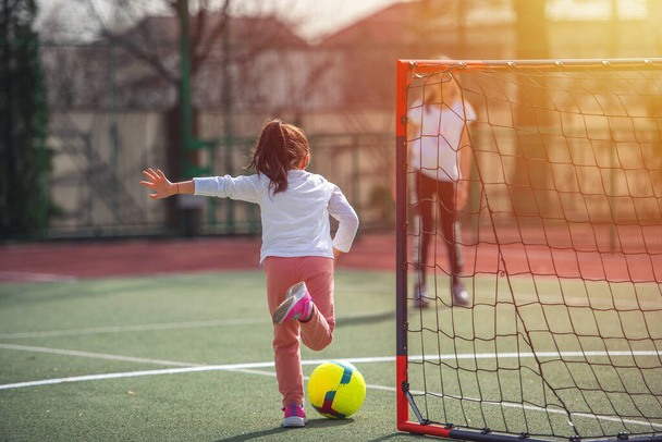 Happy little girl playing football in spring sunny day. Childhood, leisure games and people concept - Photo, Image