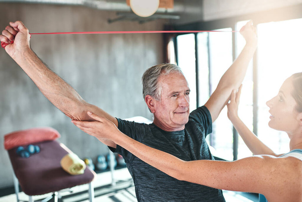 Targeting arm strength with resistance bands. Shot of a senior man using resistance bands with the help of a physical therapist. - Foto, Imagen