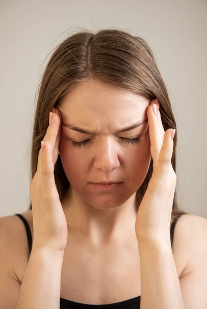 young female suffers from headache migraine holding hands near temple head - Fotografie, Obrázek