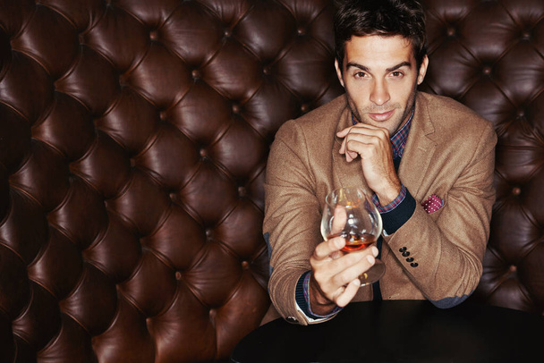 Serious about my brandy. Portrait of a handsome young man drinking in a club. - Foto, imagen
