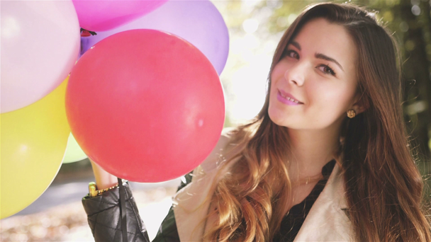 Vrolijke brunette meisje met kleurrijke ballonnen glimlachend in herfst park. - Video