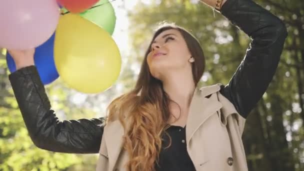 Cheerful brunette girl with colorful balloons smiling in autumn park. - Video, Çekim