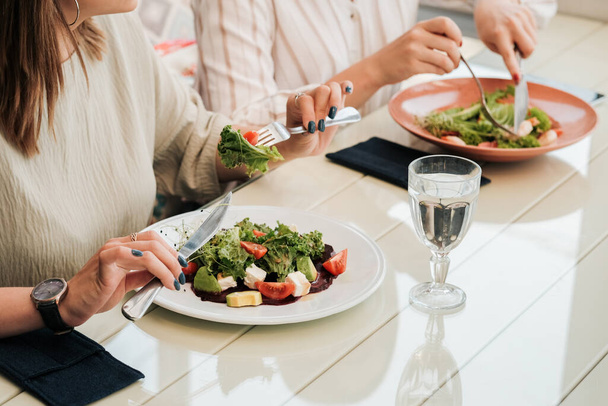 Primo piano di donne irriconoscibili che pranzano insieme, mangiano insalata nel ristorante  - Foto, immagini