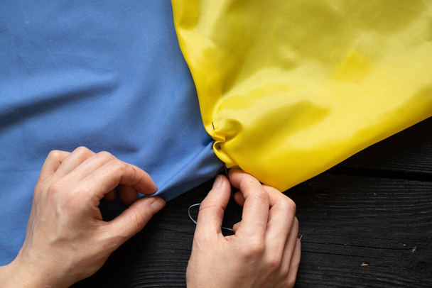 Ženské ruce ukrajinské ženy šít národní vlajku Ukrajiny žlutomodrý u stolu doma na Ukrajině, vlastenec, zastavit válku na Ukrajině 2022 - Fotografie, Obrázek