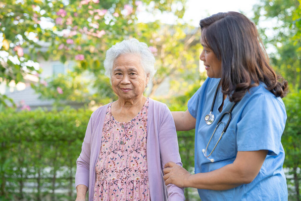 Γιατρός βοήθεια και φροντίδα της Ασίας ηλικιωμένους ή ηλικιωμένη ηλικιωμένη γυναίκα χρησιμοποιούν περιπατητής με ισχυρή υγεία, ενώ το περπάτημα στο πάρκο σε χαρούμενες φρέσκες διακοπές. - Φωτογραφία, εικόνα
