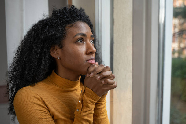 Eine schwarze Frau betet deprimiert vor dem Fenster - Foto, Bild