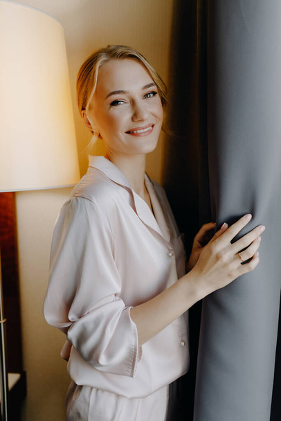  The bride stands at the window in the morning and smiles and looks at the camera. High quality photo - Valokuva, kuva