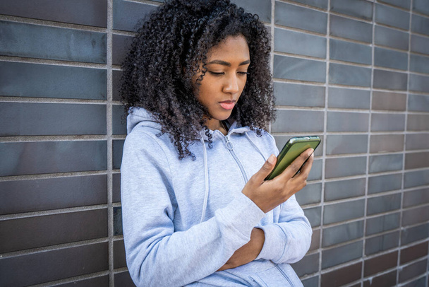 Jedna smutna młoda czarna dziewczyna smsuje samotnie przez telefon komórkowy - Zdjęcie, obraz