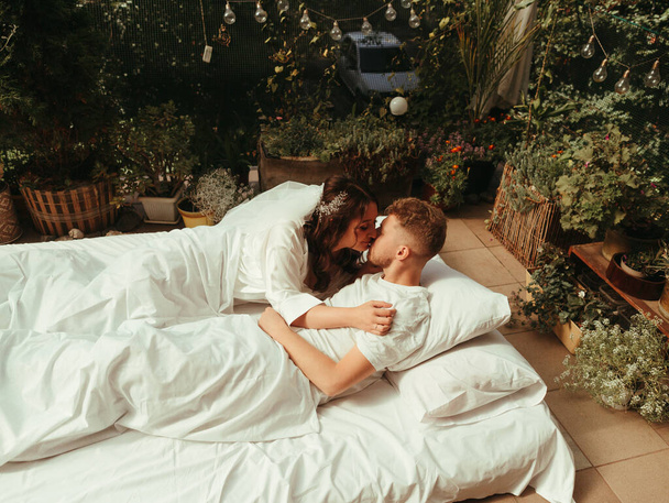 Sevgi dolu evli bir çift otelde yatağa uzanıyor, birlikte rahatlıyorlar. Bornozlu kadın ve erkek dinlenir, boş zaman geçirir, eğlenir. tahıl etkisi - Fotoğraf, Görsel
