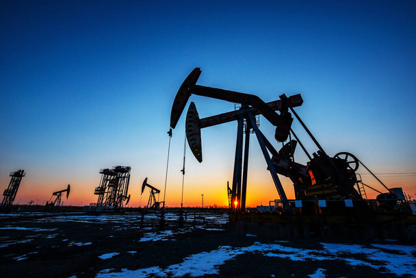 Az olajmezők olajszivattyúi este dolgoznak, az olajszivattyúk sziluettjei napnyugtakor. - Fotó, kép