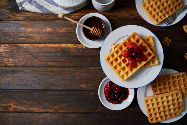 Kahvaltı waffle 'ları çilek, yabanmersini, ahududu, bal ve ahşap masada fındık ile servis edilir. Üst görünüm. - Fotoğraf, Görsel