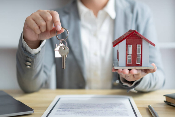 Concepto de seguro el representante de bienes raíces sosteniendo una llave de la casa en la mano derecha y el modelo de la casa en la mano izquierda. - Foto, Imagen