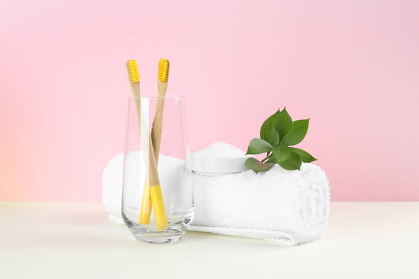 Bamboo toothbrushes, towel and bowl of baking soda on beige table against pink background - Foto, Bild