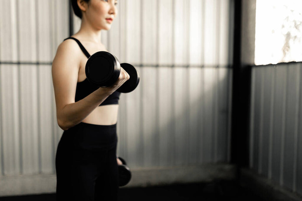 Концепция упражнений Прочная женщина поднимает два гантели в руке и делает сосредоточенность кувырка справа, стоя. - Фото, изображение