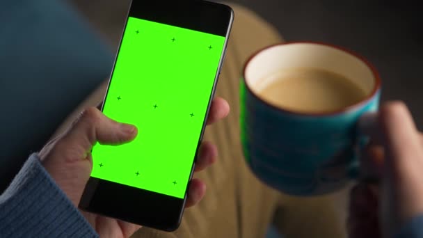 Hombre usando smartphone con pantalla verde simulada en modo vertical y bebiendo café. Hombre navegando por Internet, viendo contenido, videos. - Imágenes, Vídeo