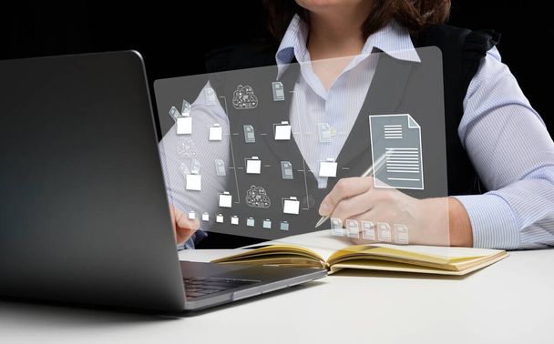 Μια γυναίκα κάθεται σε ένα τραπέζι και δουλεύει με ένα λάπτοπ. Σύστημα διαχείρισης εγγράφων (DMS). Λογισμικό αυτοματοποίησης αρχειοθέτησης και αποτελεσματικής διαχείρισης αρχείων πληροφοριών - Φωτογραφία, εικόνα