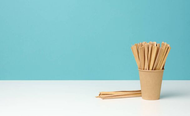 vasos de papel desechables y palos de madera en la mesa blanca, fondo azul, espacio de copia - Foto, imagen