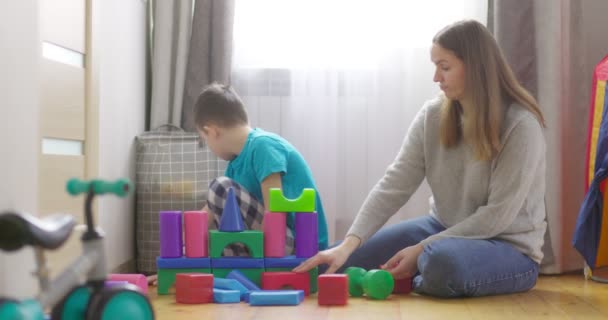 Mère avec son fils jouant avec des cubes colorés assis sur le sol à la maison. Famille passe du temps ensemble à la maison dans la chambre des enfants. - Séquence, vidéo