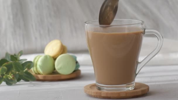 Le sucre est versé d'une cuillère dans une tasse transparente de café avec du lait, au ralenti. Ajouter du sucre à la tasse de café, cuillère est en remuant le sucre dans une tasse - Séquence, vidéo