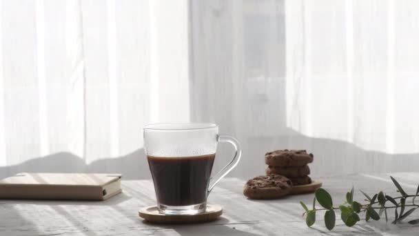 Pára horký šálek kávy v ranních stínech a slunečních paprscích oknem na šedém pozadí stolu. Horký průhledný skleněný šálek na kávu s parním zoomem. Hot Coffee Drink koncept - Záběry, video