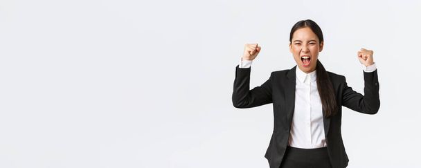 Successful winning businesswoman fist pump and shouting yes from happiness and delighted, achieve goal, celebrating victory, triumphing over prize, standing white background - Photo, Image