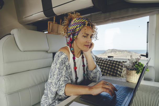 キャンパーバンの代替オフィス内のラップトップコンピュータを使用して魅力的な若い大人の女性。人々やデジタル遊牧民やスマート作業活動ライフスタイル。ヴァンライフと仕事のための旅行。オンライン仕事活動 - 写真・画像