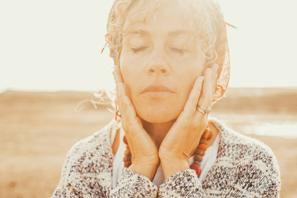 Πορτρέτο της ενήλικης γυναίκας με κλειστά μάτια και τα χέρια στο πρόσωπο. Η στιγμή της αγάπης και των συναισθημάτων. Άνθρωποι και ευημερία δραστηριότητα διαλογισμού σε εξωτερικούς χώρους με χρυσό φως ηλιοβασίλεμα στο παρασκήνιο - Φωτογραφία, εικόνα