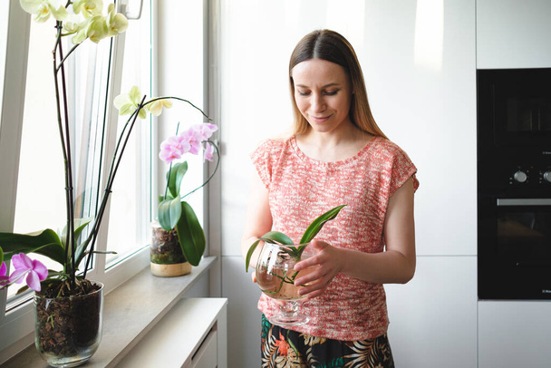Mulher bonita que segura nas mãos uma lata de água com uma planta do orchid
 - Foto, Imagem