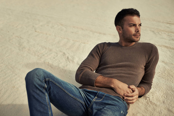 Se ve elegante en el desierto. Un guapo modelo masculino reclinado en la arena del desierto con ropa de moda. - Foto, imagen