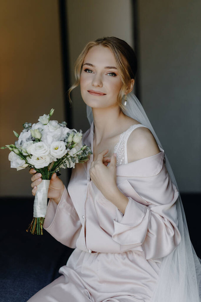  Beautiful bride in pajamas sits on a bed with a bouquet. High quality photo - Photo, Image