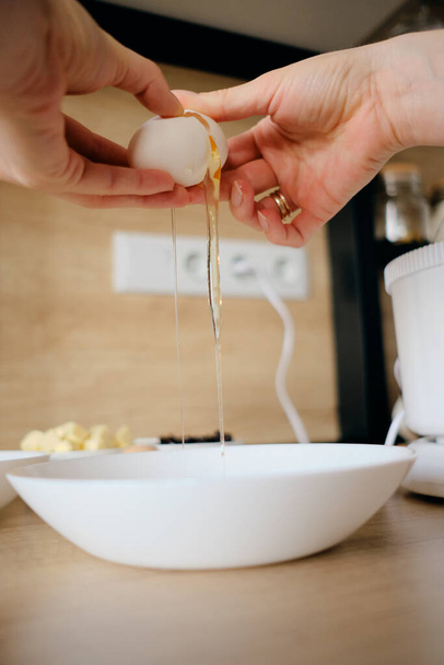 Le mani della donna rompono le uova di pollo in una ciotola in cucina. - Foto, immagini