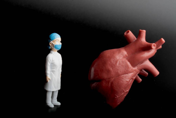 μικροσκοπικό ειδώλιο καρδιολόγου γιατρού με τεράστια ανθρώπινη καρδιά σε μαύρο φόντο - Φωτογραφία, εικόνα