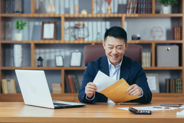Portrait of a successful businessman, Asian received a letter of approval from the bank, to extend the credit line, a happy man working at the table, holding an envelope - Фото, зображення