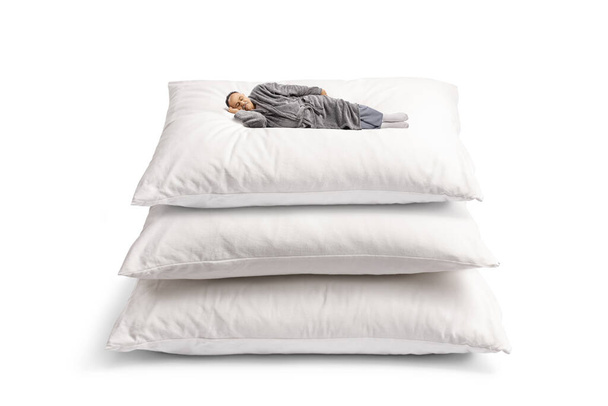 Man in a bathrobe sleeping on a pile od giant pillows isolated on white background - Fotó, kép