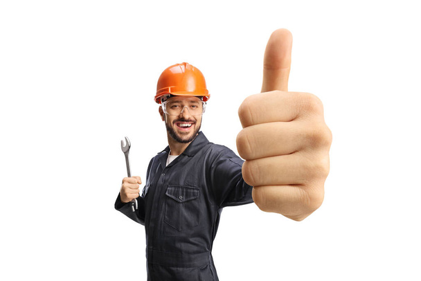 Worker in a uniform with helmet holding showing a thumb up gesture isolated on white background - Foto, afbeelding