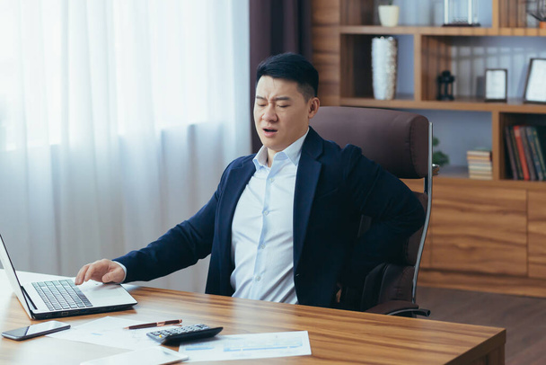 Businessman working in the office at the computer, Asian has severe back pain, boss in a classic office, reworked - Фото, зображення