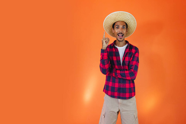 Чернокожий человек с джунинским партийным костюмом на оранжевом фоне. Молодой человек в традиционной одежде для фестиваля Festa Junina - Бразильский июнь. - Фото, изображение