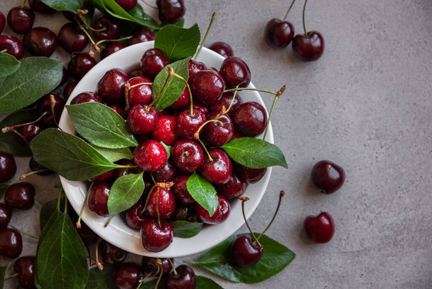 Fresh ripe dark cherries with green leaves  - Фото, изображение
