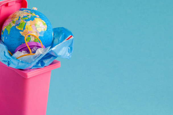 Creative ecological composition. The garbage can is filled with plastic bags, rubber, and plastic tubes. Pastel blue background. Protect our environment, use paper bags. Copy space - Foto, immagini