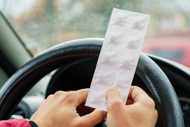 Tablettenpackung in den Händen des Fahrers auf einem verschwommenen Hintergrund des Lenkrads im Auto. Die Verwendung pharmakologischer Medikamente für medizinische Zwecke während der Fahrt. Selektiver Fokus - Foto, Bild