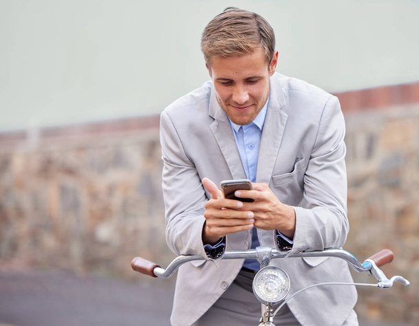 I cant believe she texted me. Shot of a young businessman using his smartphone while riding a bicycle. - Фото, изображение