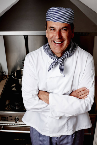 Senior chef with hands folded standing in front of vent hood. Portrait of a cheerful senior chef with hands folded standing in front of vent hood. - Foto, Imagem