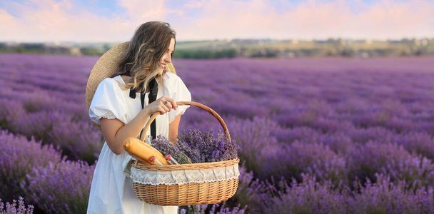 Beautiful young woman with basket for picnic in lavender field - Φωτογραφία, εικόνα