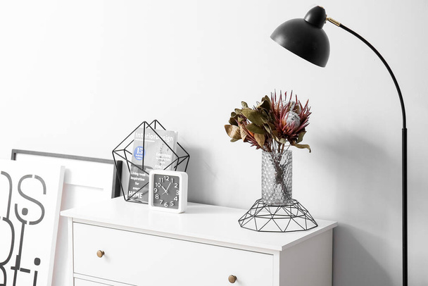 Váza s květinami, zásobníkem a hodinami na zásuvce u světelné stěny - Fotografie, Obrázek