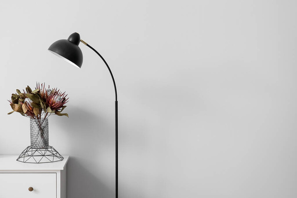 Ваза с цветами на полке и черная стоячая лампа возле светлой стены - Фото, изображение